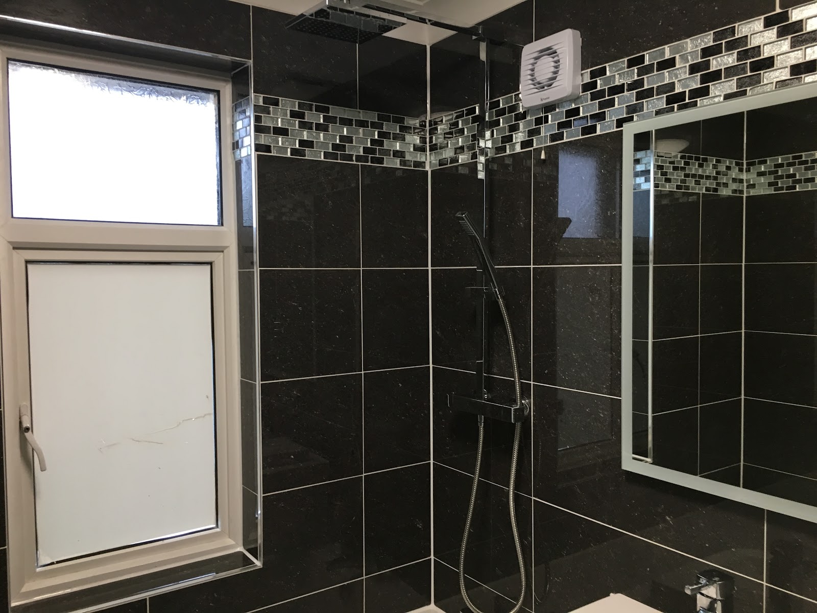 A finished bathroom with black porcelain tiling, mosaic border and thermostatic shower