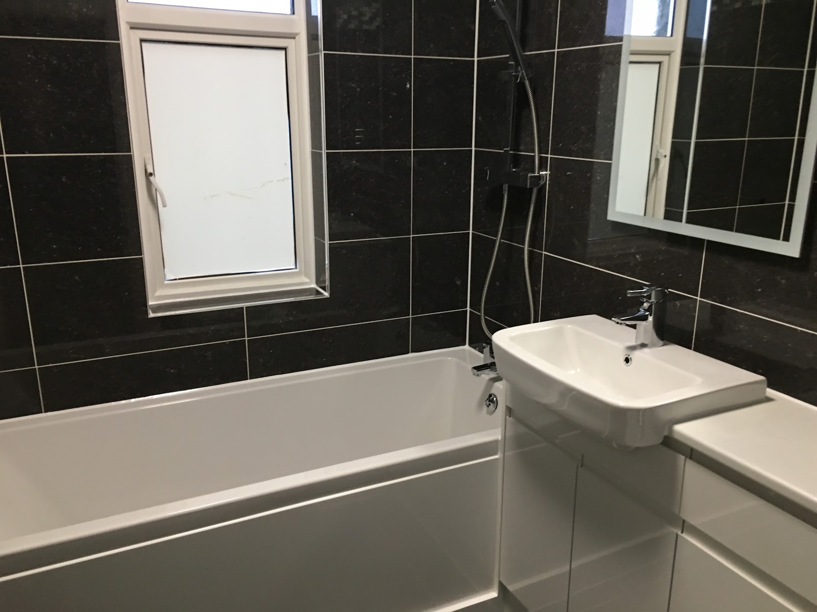 A completed family bathroom with dark tiling, bath, basin and mirror